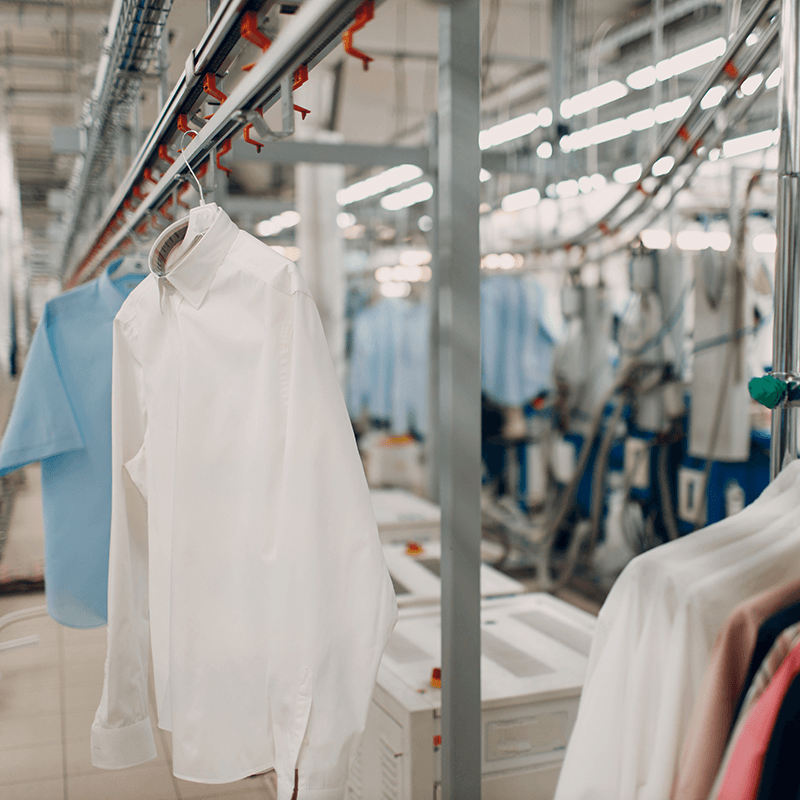 Shirts hang from racks at drycleaning facility.