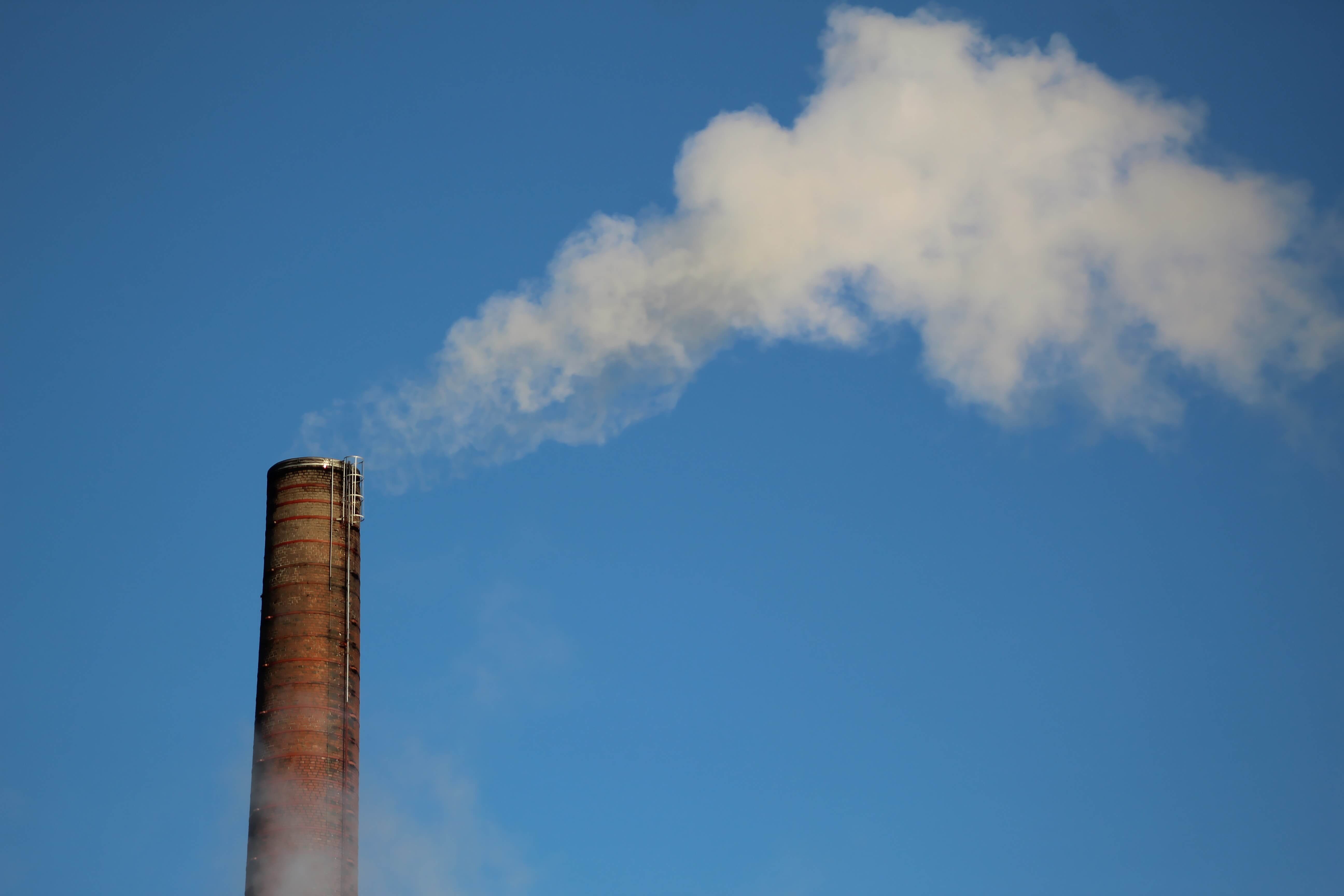 brown chimney releasing air from a factory into the blue sky