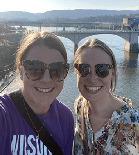 two young women posing in front of bridge