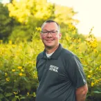 man in gray shirts standing in font of prairie with yellow flowers