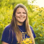 Environmental intern Jordan Burrows stands before a field of yellow flowers.