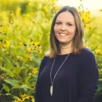 Staff member Jen Wittenburg stands before a field of yellow flowers.