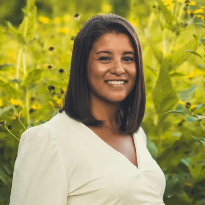 Link, Molly Wells standing before field of yellow flowers, profile page